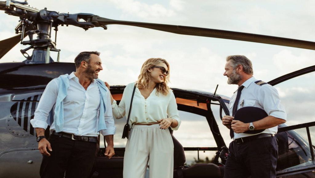 Smiling couple alighted from a private helicopter talking to the pilot. Couple getting off a private aircraft with mature pilot. (Smiling couple alighted from a private helicopter talking to the pilot. Couple getting off a private aircraft with mature